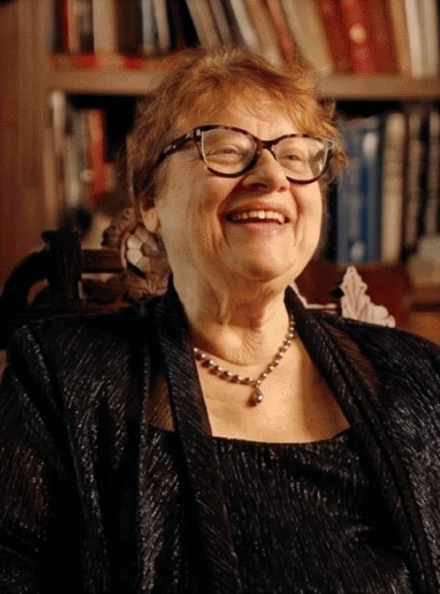Janice Stauffer laughing, seated in front of a bookshelf